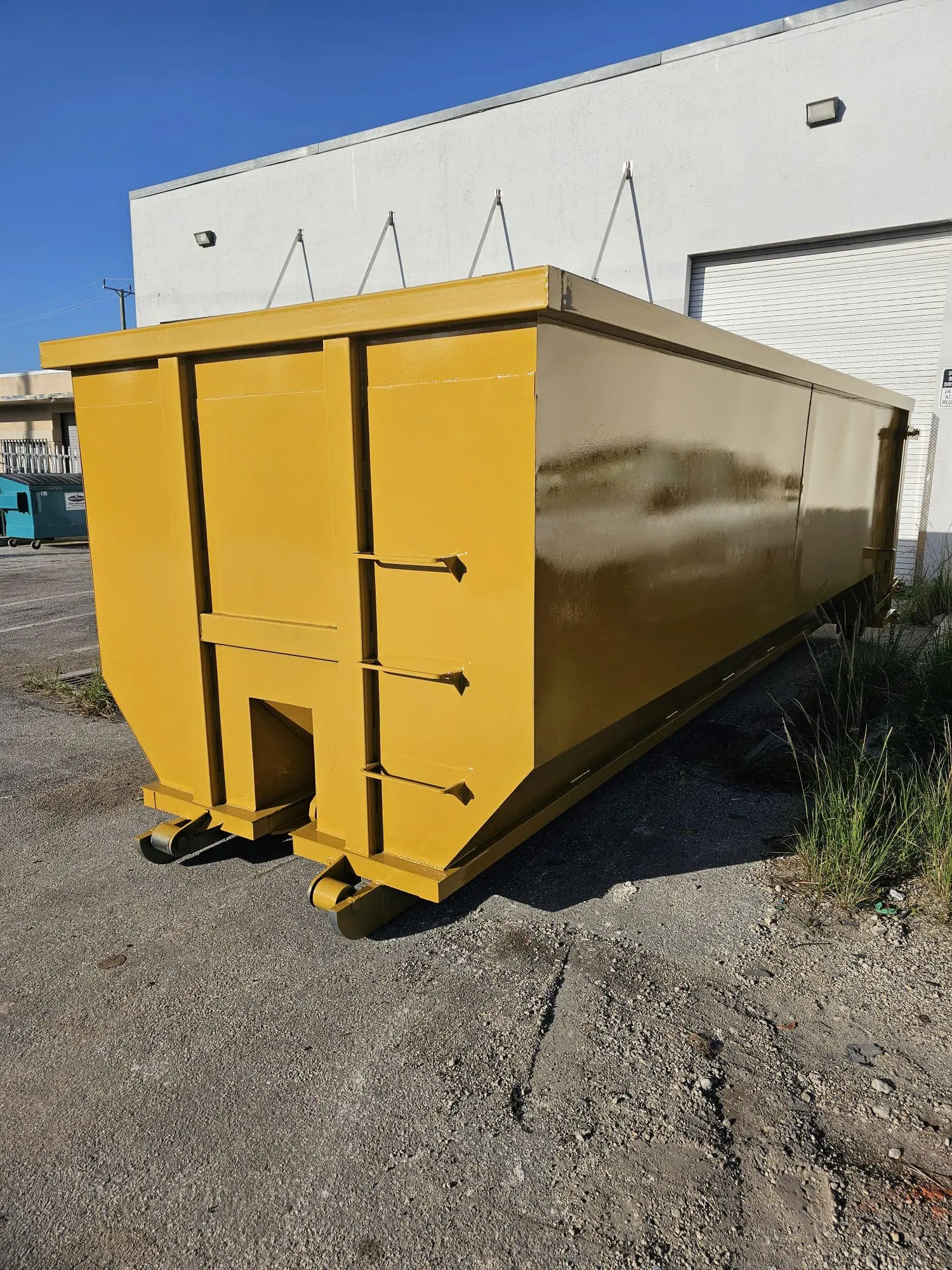 Large yellow commercial dumpster sitting on asphalt outside a white warehouse