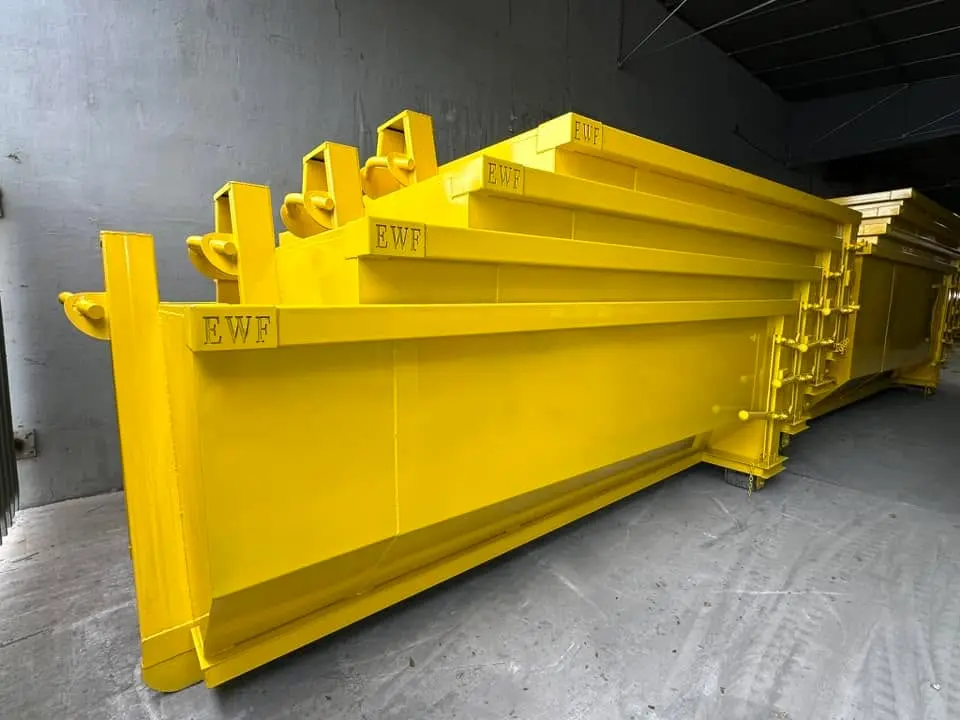 Row of yellow dumpsters with reinforced hooks neatly stacked on concrete floor