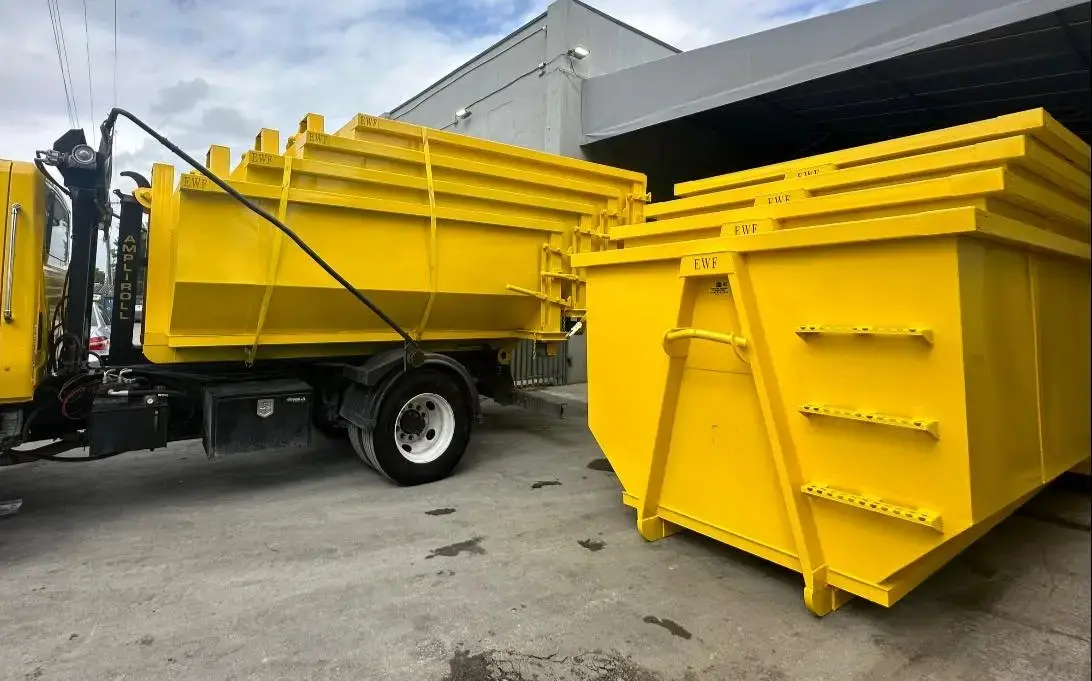 Commercial dumpster rental truck hauling multiple yellow bins in a stack at an industrial site, ready for delivery or pickup