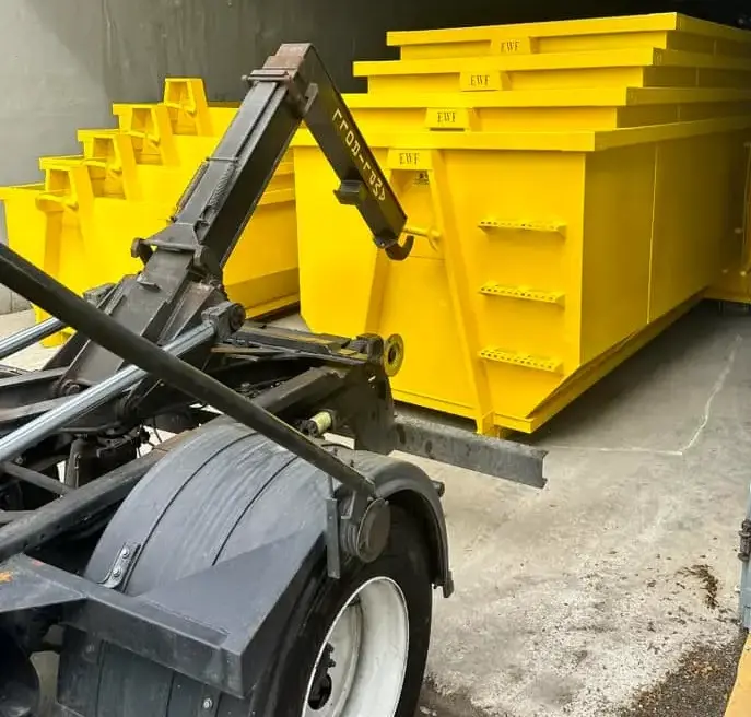 Hydraulic arm truck adjacent to several yellow dumpsters lined up for deployment
