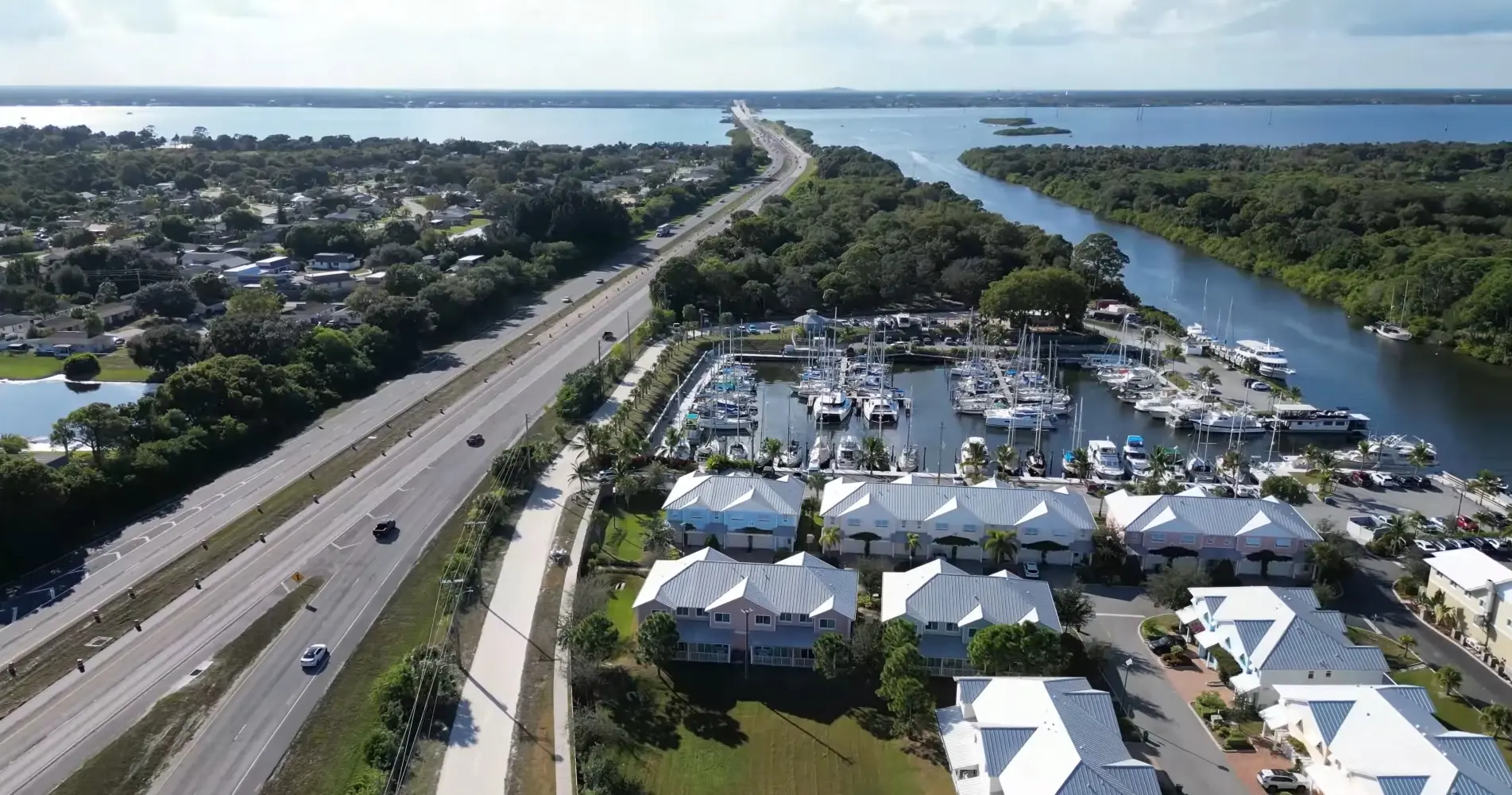 Merritt Island reveals marina docks lined with yachts beside a tree-lined highway and residential units, photographed by Space Coast Dumpster Rental