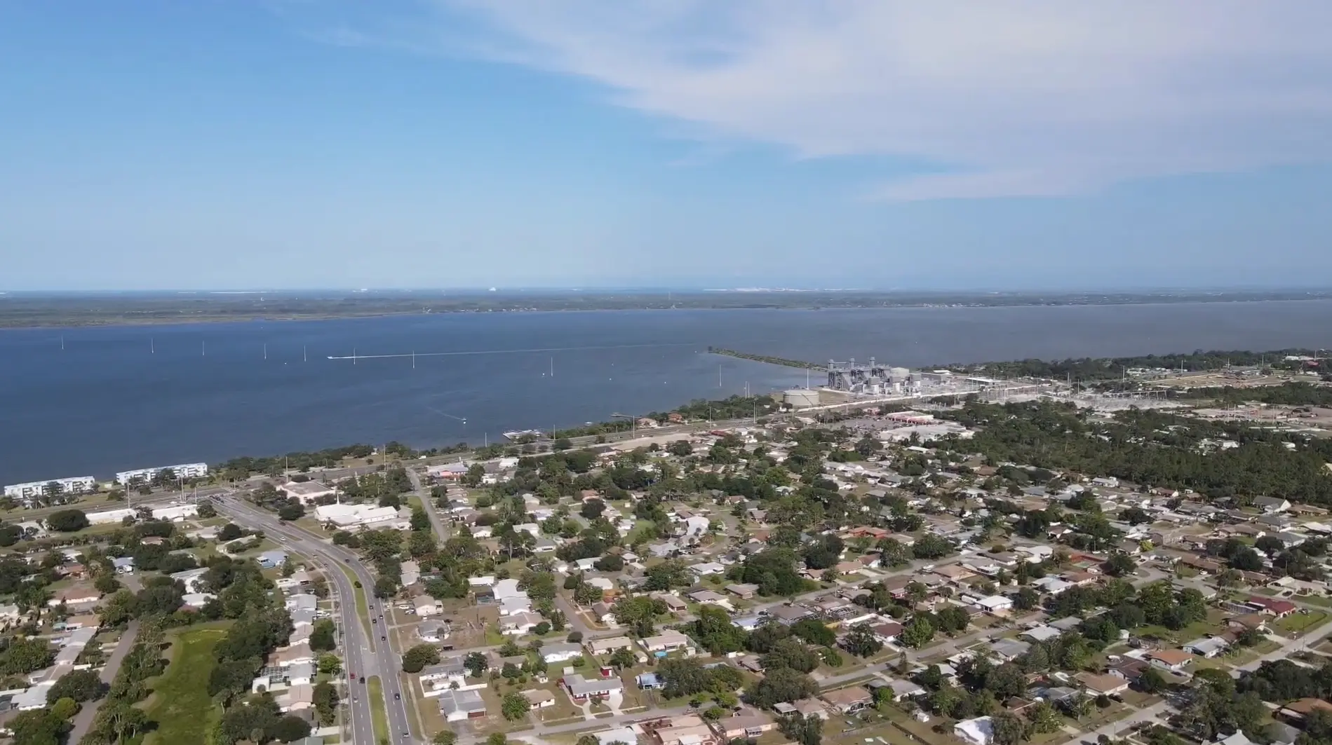 Port St. John displays a sprawling residential grid bordering the wide Indian River under a clear sky, captured by Space Coast Dumpster Rental