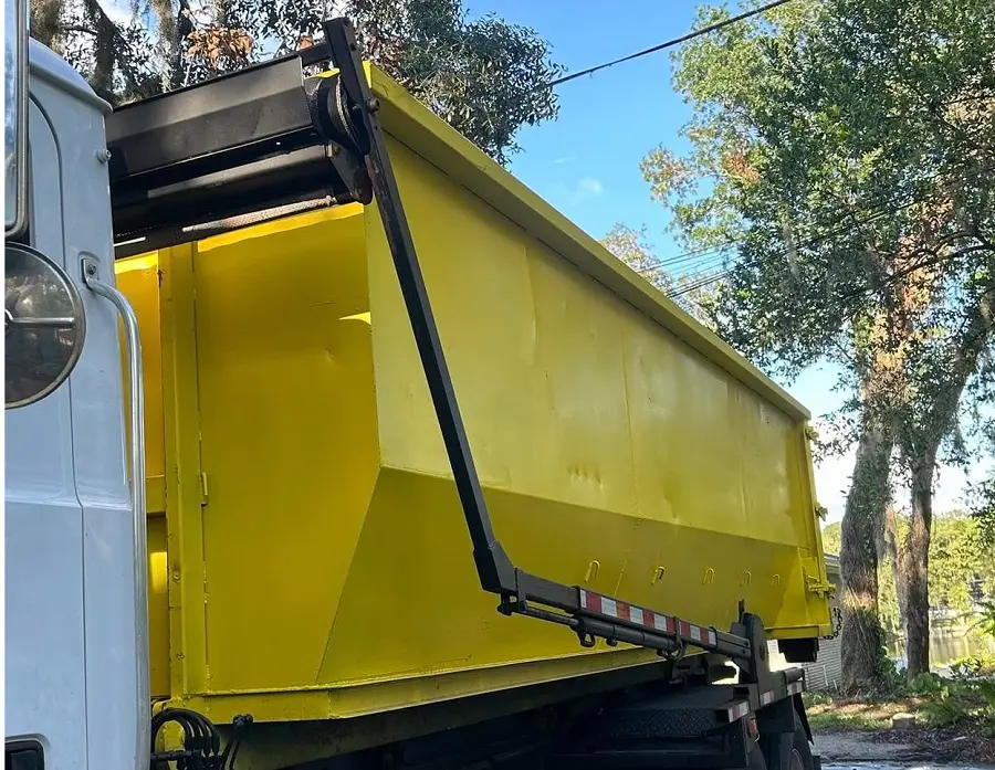 Residential dumpster rental by Space Coast loads yellow dumpster onto tilt truck in driveway