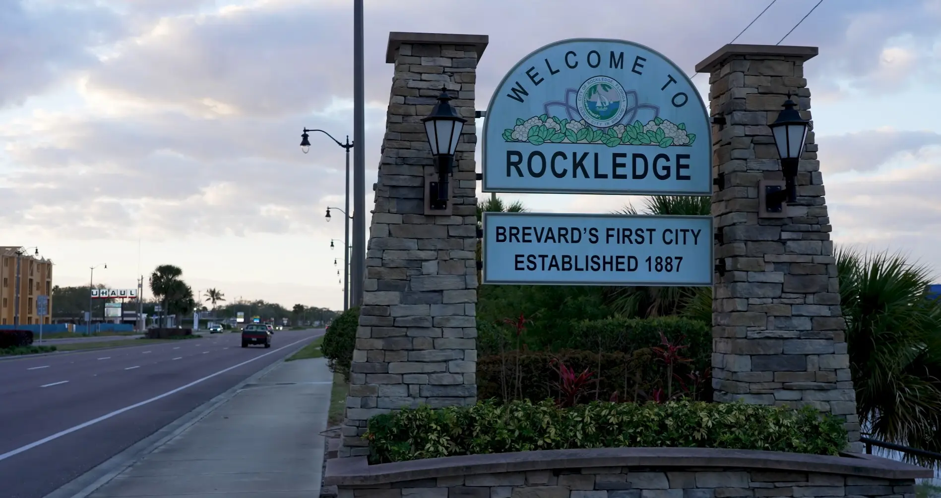Rockledge welcomes drivers with a stone gateway sign along a multi-lane road bordered by palm trees, captured by Space Coast Dumpster Rental