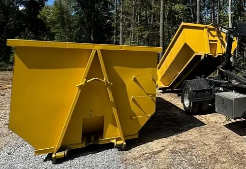 Space Coast Dumpster Rental unloads a yellow roll-off dumpster beside another container near a wooded area